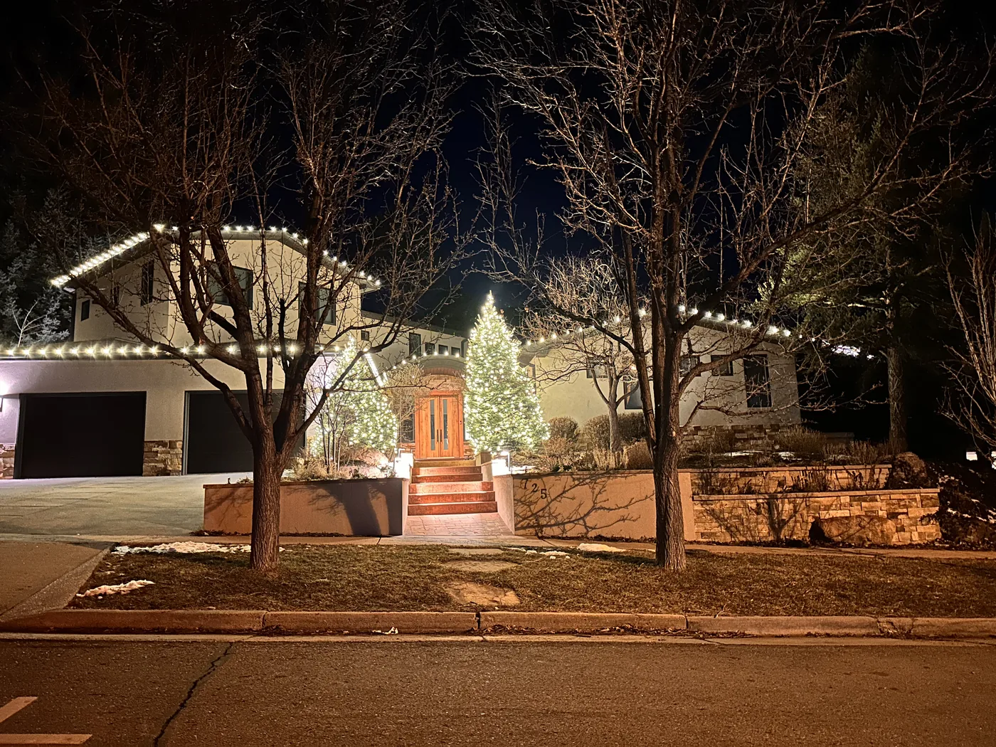 A Boulder home in warm white with a fully lit evergreen beside the entry