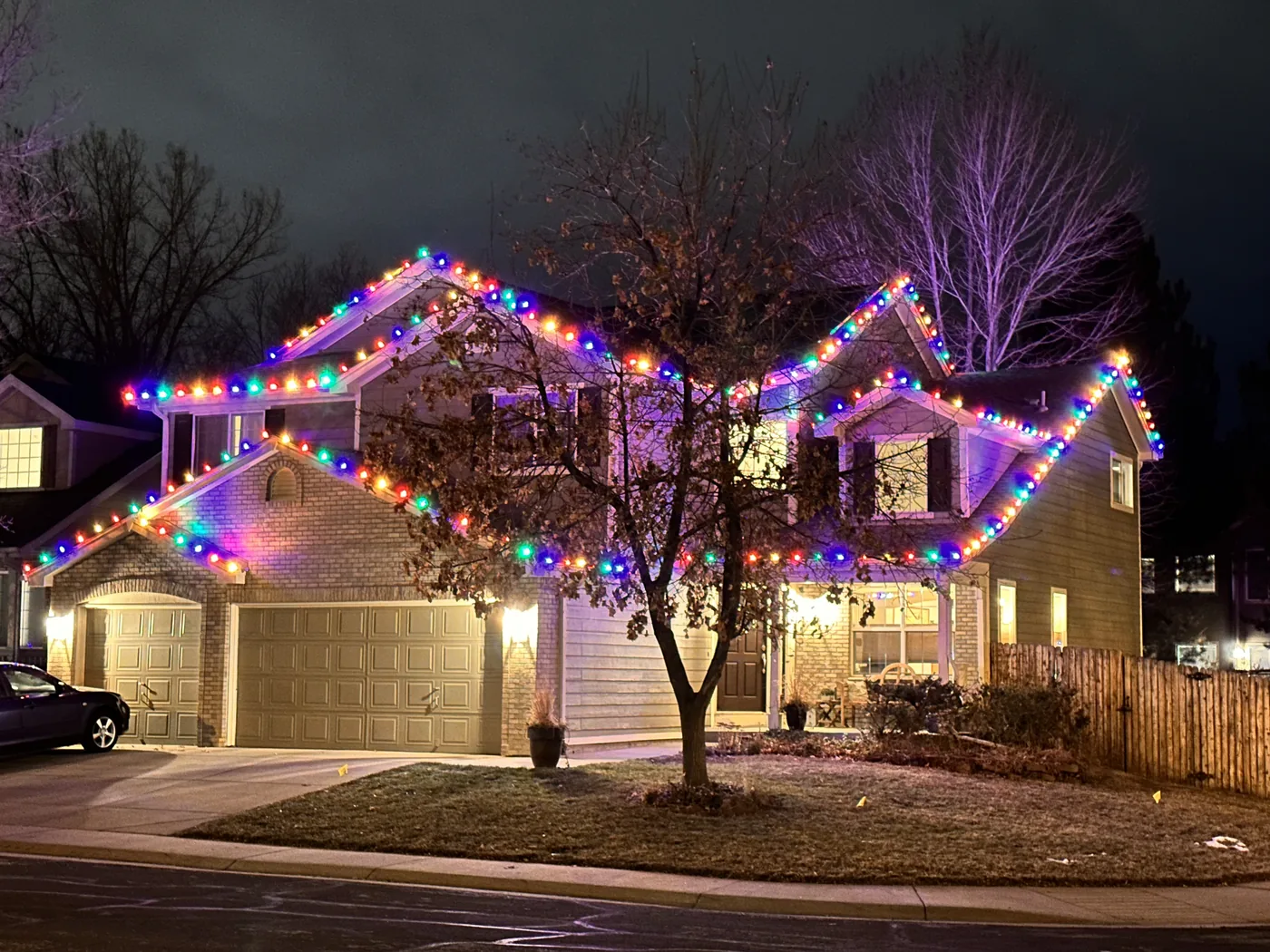 A Broomfield home with multicolor bulbs along every gable and colored uplighting on the facade