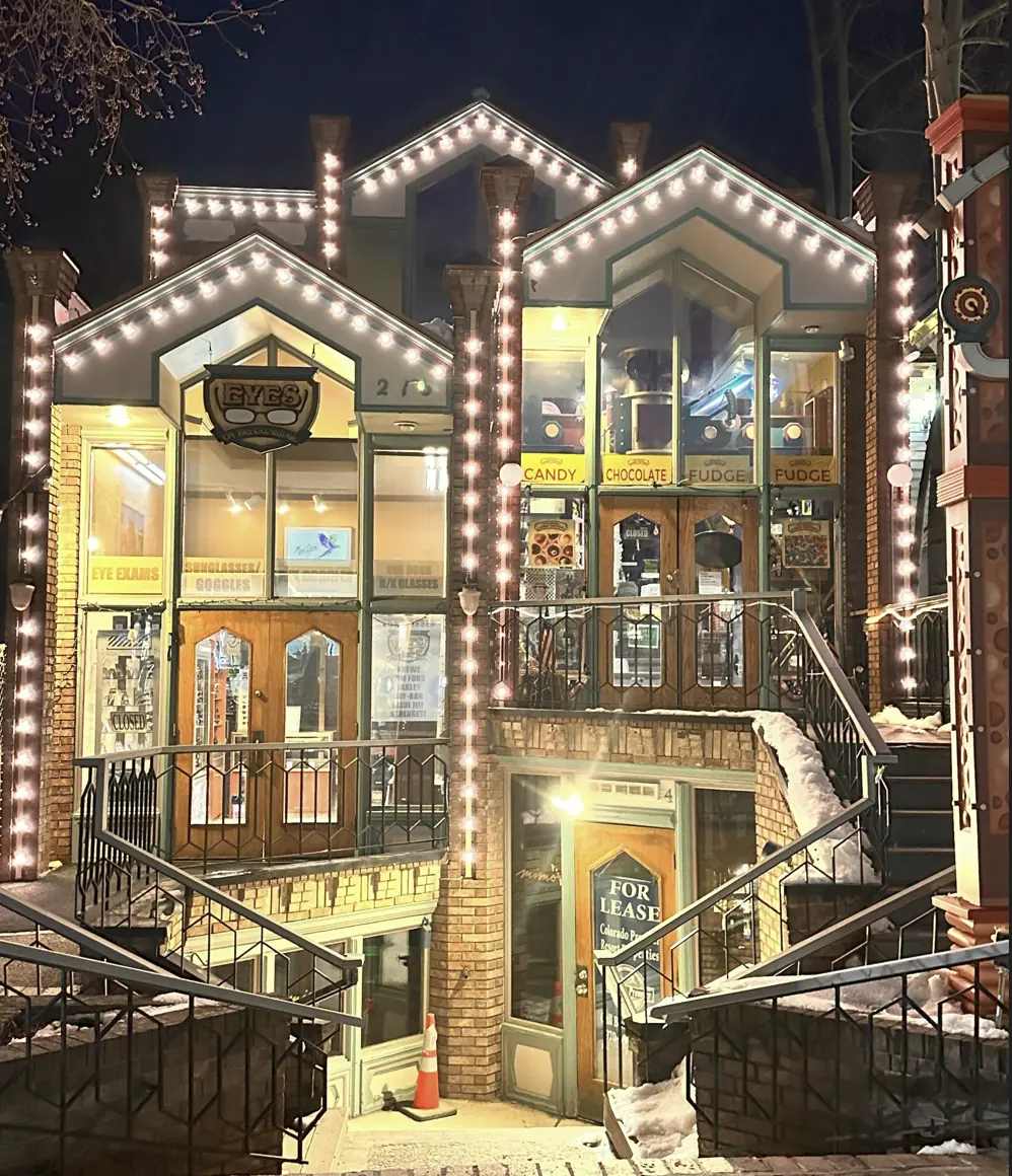 Two-story retail building with every gable, column and stair rail traced in warm white bulbs at night