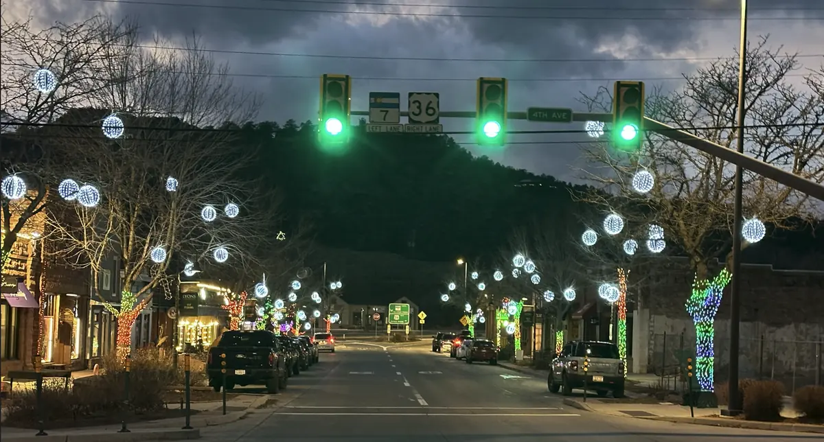 Lyons Main Street at dusk with lit spheres in the street trees and color-wrapped trunks leading toward Sandstone Park
