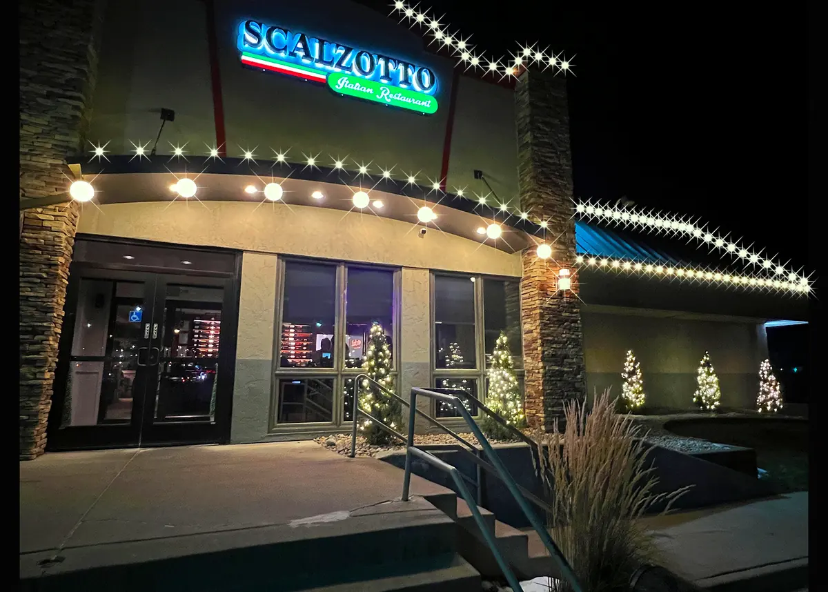 Scalzotto Italian Restaurant entrance with C9 bulbs along the parapet and lit potted evergreens flanking the walk