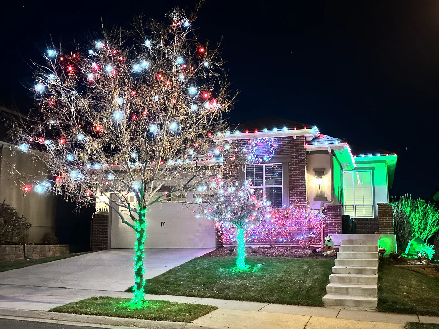 A Firestone home with a fully wrapped front tree in pink and green beside a lit roofline