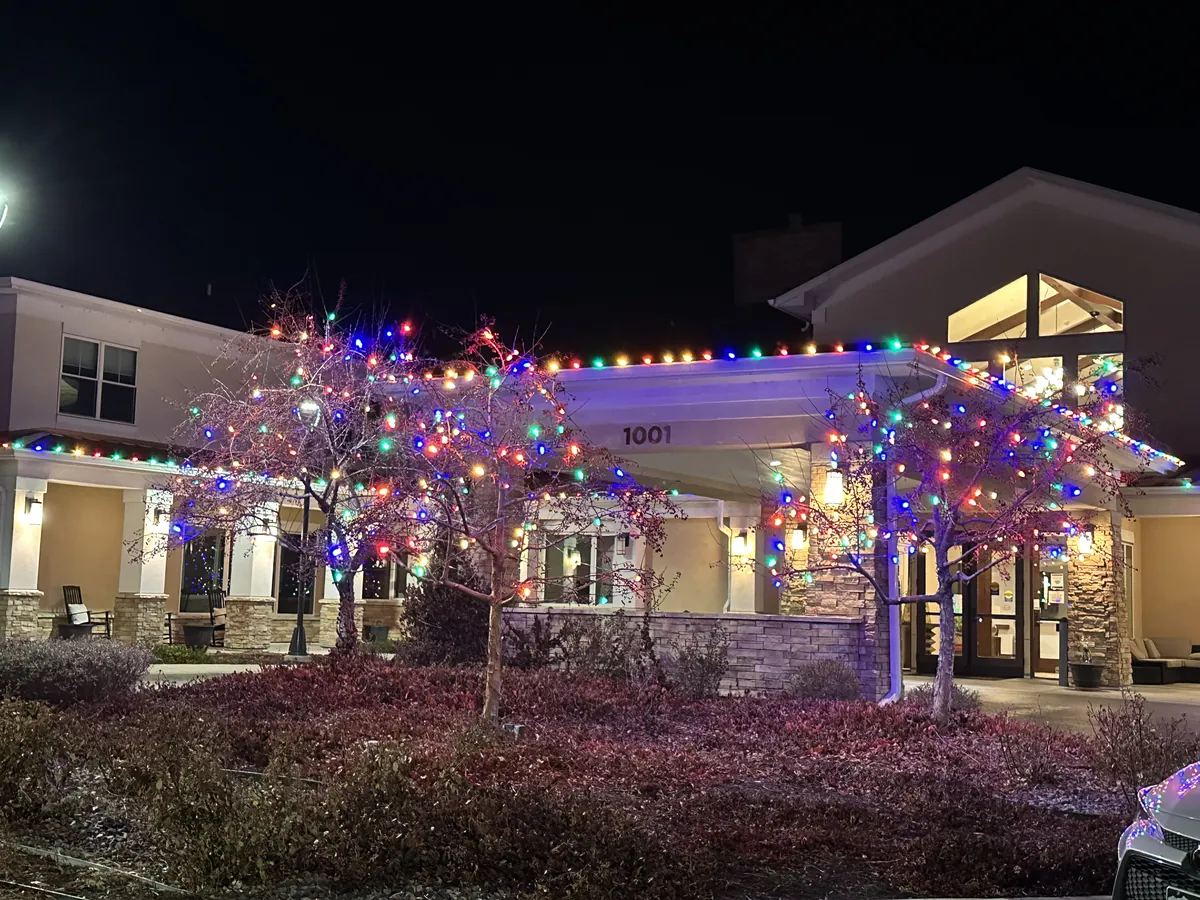 A Longmont senior living community lit in multicolour along the frontage with wrapped entry trees