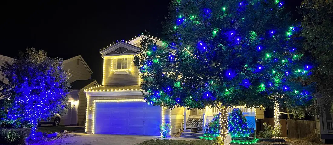 Home with warm white roofline lighting and blue and green lit trees