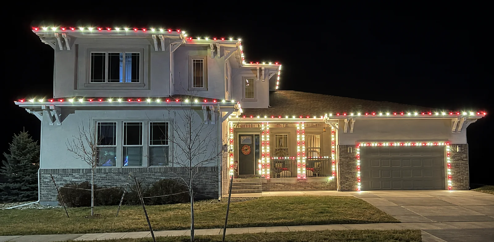 A Longmont two-story home outlined in red and white C9 bulbs along every roofline, with candy-cane wrapped porch columns and a lit wreath on the door