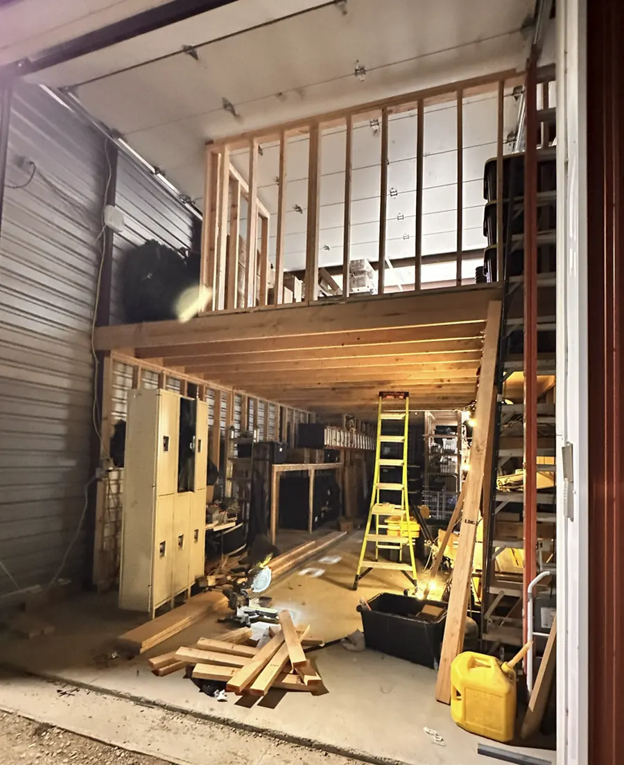 A Family Holiday Lighting warehouse bay with a new timber mezzanine, racked storage totes, ladders and a saw bench